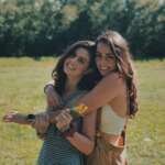 Two smiling sisters embracing in a sunlit park, enjoying a warm summer day together.